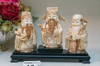 Three carved bone figurines on black wooden stand, arranged left to right