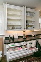 Kitchen cabinets open showing white plates and bowls, kitchen appliances on granite countertop