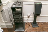 Stereo console on stand with one speaker on stand and two remotes on top