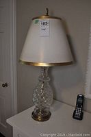 Full view of the crystal table lamp with white shade and gold trim on a white dresser.