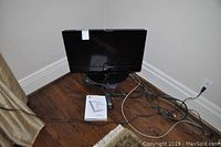 LG 26-inch TV with base stand, remote control, and user manual on hardwood floor with cables visible.