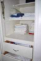 Shelves with folded linens including pillowcases, sheets, and a bolster pillow cover in white and navy blue.