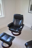 Front view of black leather chair and ottoman on wood bases