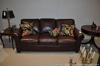 Front view of brown leather sofa with three floral print pillows and side tables.