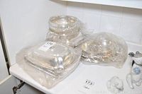 Rectangular silver plated serving dish with lid wrapped in plastic on countertop.
