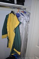 Green and yellow rain jacket hanging in closet on a black hanger.