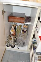 View inside cabinet shelf showing two beer steins, wooden box, two figurines, Harman Kardon tube speakers with cords, and a larger transparent dome speaker.