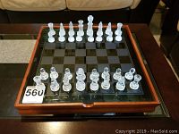 Glass top wood chessboard with clear and frosted glass chess pieces arranged ready for play.