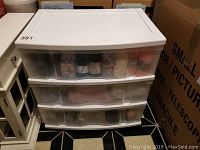 Photo of three white rolling storage drawers filled with various colors of wool yarn, view from front with drawers closed.