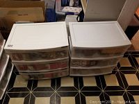 Two white plastic rolling storage drawer units on floor, each with three transparent drawers showing contents of Christmas bows, ribbon, and craft supplies