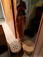 Photo showing scarecrow standing behind wooden apple basket, lidded round wood box, and bulb starter trays