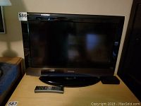 Front view of the Toshiba TV showing its black frame and the base stand, with two remote controls on the table in front of it.