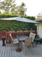 Photo of patio set including glass table, chairs and large green umbrella on cast iron base, showing overall setup on deck