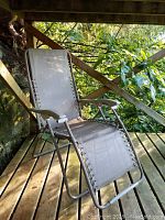 Beige zero gravity chair angled on wooden deck outdoors, showing fabric seat and metal frame.
