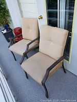 Two beige cushioned aluminum patio chairs side by side on a porch