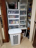 Photo of stacked plastic drawer storage units including one four-drawer and two three-drawer units, with a white hamper in front.