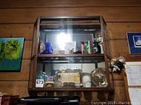 Front view of the curio cabinet displaying glass shelves with various objects inside, wood walls background