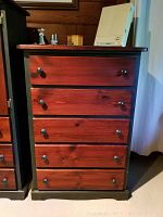Front view of a five-drawer dresser showing mahogany colored drawers with dark round knobs and forest green base and sides, wood grain visible.