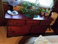 View of mahogany top surface with several potted plants and a fan, showing dresser's wood grain and finish.