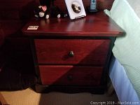Night stand with two drawers next to bed, showing dark wood finish with black trim and drawer knobs