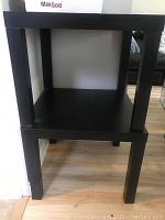 Front view of one black side table showing the square top and bottom shelf with four legs.