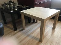 Two side tables in a room with wooden floor. Light beige and black colors, square shape, straight legs.