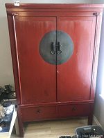 Full front view of the red Asian themed wooden side cabinet with closed doors and drawer below.