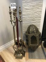 Full view of brass fireplace tool set with stand consisting of brush, shovel, poker, and tongs next to the Moroccan brass lamp.