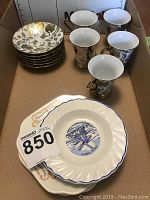Ironstone plates stacked with detailed edging and central blue design. Four white espresso cups next to ornate silver holders in cardboard box.
