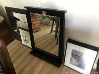 Photo of large dark wood framed mirror with drawer, leaning against wall.