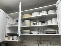 Cabinet with multiple shelves holding white Corningware bowls, ramekins, plates, and mugs.