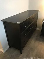 Black wooden chest of drawers, side angle showing full length and height.