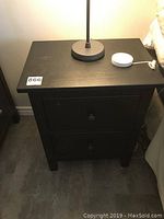 Full view of one black wooden side table with lamp and smart home device on top.