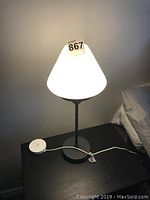First lamp lit on black wooden table with white glass shade and dark metal base. A round white foot switch is seen on the cord.