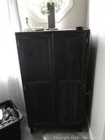 Front view of the dark wooden storage cabinet with closed doors and objects on top.