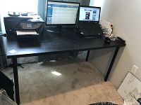 Full view of black rectangular IKEA table with some office equipment placed on top, rectangle shape, four legs.