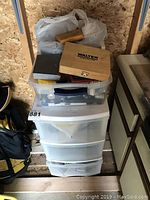 Photo showing three stacked white plastic storage drawers with items on top including a wooden Walter branded drill bit set case and a bag with other items.