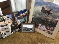 Three framed prints on carpet, including military helicopter scenes and a black and white cityscape photo.