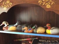 Five wooden decoy ducks on shelf showing differing sizes, colors, and markings.