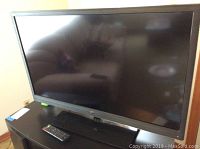 Front view of the Westinghouse flat screen TV with black frame, screen off. Remote control placed in front of the TV on a stand or table.