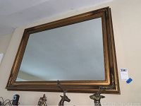 Large gold framed wall mirror mounted on wall, showing reflective glass and frame visible.
