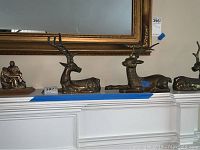 Wide shot showing all three brass deer and the brass Pieta figurine arranged on a shelf under a framed mirror.