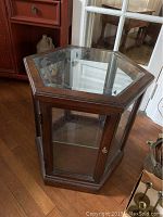 Full view of hexagonal wooden display cabinet with glass top and front glass door.
