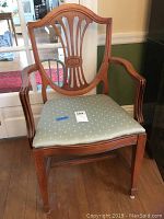 Cherry wood arm dining chair with curved back featuring vertical slats and an oval medallion, upholstered light blue cushion with diamond pattern.