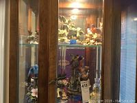 Two glass cabinet shelves displaying multiple bird statues in various poses and colors.