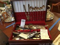 Box open showing interior red and white fabric lining with some flatware in slots and more loose inside.
