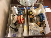 Overhead view of various bird figurines, including blue Goebel birds, turkey salt and pepper shakers, marble duck, rooster, Mini Lefton bird, and other small collectibles arranged in two trays.
