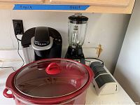 Photo showing Keurig coffee maker, Crockpot slow cooker with glass lid, Black & Decker blender, and electric knife sharpener on countertop.