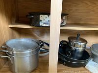 Wide view of multiple pots, pans, and an enamel roaster in wood cabinet shelf