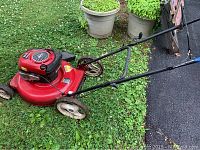 Side angled view of red Craftsman lawn mower on grass showing engine housing, wheels, and handlebar in detail.